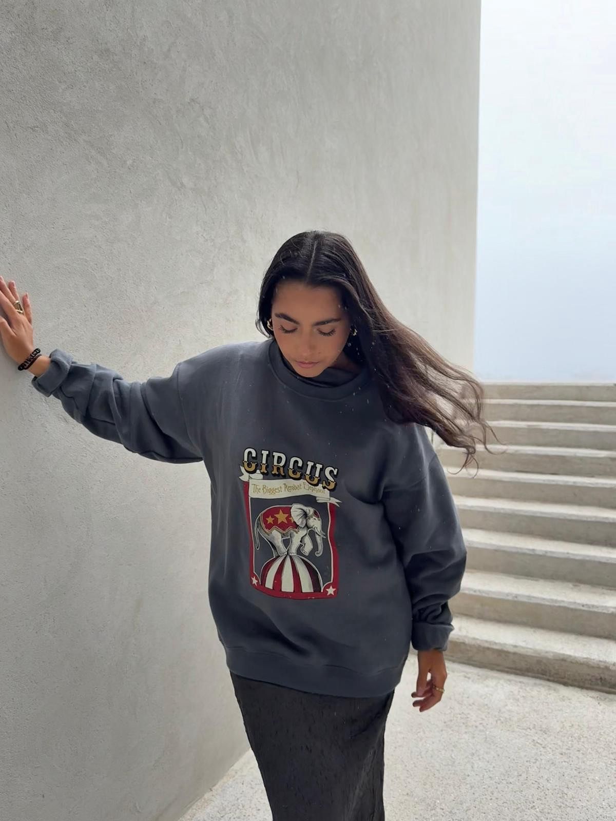 Mujer apoyada en una pared con sudadera gris azulado eleOnora y estampado de elefante de circo